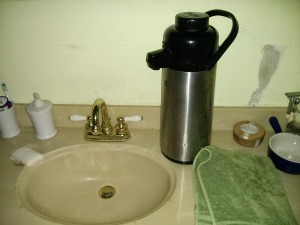 A sink with a carafe full of hot water. 